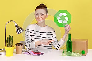 Woman manager holding recycling sign and pointing at plastic, glass bottles and cardboard package.