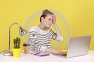 Woman manager sitting at workplace with laptop and keeping hand on forehead, blaming herself.