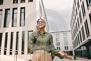 Woman manager talking phone with client whiile standing on modern building background