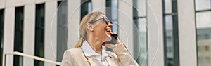 Woman manager talking phone whiile standing on modern building background and drinking coffee