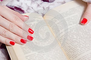 Woman manicured hand with red nails and book