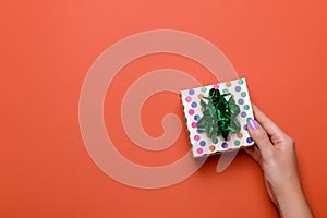 Woman manicured hands holding green giftbox on dark orange background, copy space, top view, flat lay. Giving presents or shopping