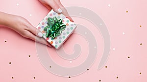 Woman manicured hands holding green giftbox on pastel pink background with confetti, copy space, top view, flat lay. Giving