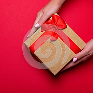 Woman manicured hands holding red and golden wrapped present or gift box on deep red background, copy space, top view