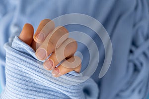 Woman manicured hands, stylish beige nails. Closeup of manicured nails of female hand in blue sweater in blue background