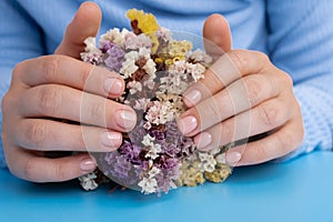 Woman manicured hands, stylish beige nails. Closeup of manicured nails of female hand in blue sweater in blue background