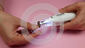 Woman is manicuring her nails using electric device with fine-grained sapphire disk and protective cap for nail dust