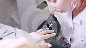 Woman manicurist in a beauty salon applies violet gel polish to the nails of a client.