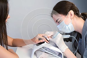 Woman manicurist in mask cleaning pterygium on client`s nail using apparatus. photo