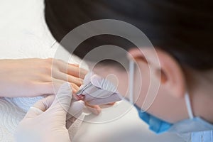 Woman manicurist master is removing cuticle and pterygium using pusher.