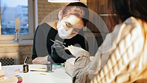 Woman manicurist in medical mask doing manicure in beauty salon