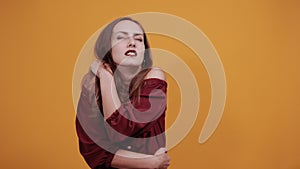 Woman in maroon dress on orange background in studio having pain in muscules.