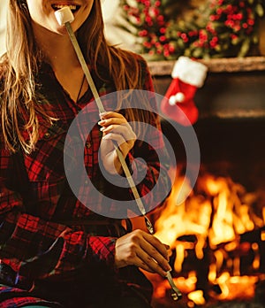 Woman with marshmallow by the fireplace. Young woman smiling and