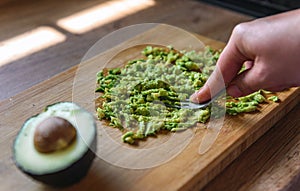 Woman mashing avocado with a fork on a wooden board