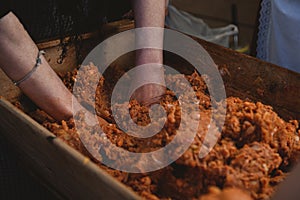 Woman mashing meat with hands in a wooden pot under the lights with a blurry background