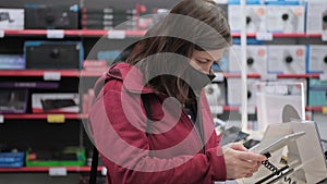 Woman in mask against virus buys new gadget in device store