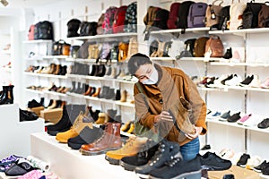 Woman in mask choosing boots in shoeshop
