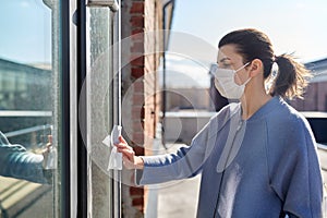 Woman in mask cleaning door handle with wet wipe