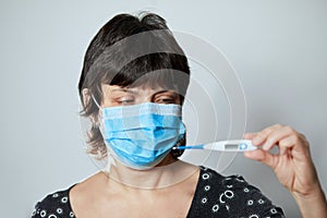 Woman in a mask with Coronavirus reads his temperature on a thermometer. Female measures the temperature.