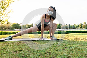 Woman with a mask doing a yoga pose while stretching the leg outdoors