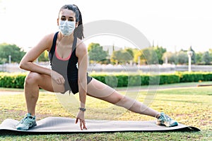 Woman with a mask doing a yoga pose and stretching the leg outdoors