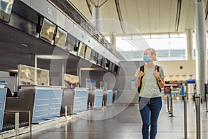 Woman in mask at empty airport at check in in coronavirus quarantine isolation, returning home, flight cancellation