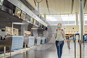 Woman in mask at empty airport at check in in coronavirus quarantine isolation, returning home, flight cancellation