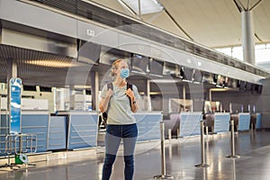 Woman in mask at empty airport at check in in coronavirus quarantine isolation, returning home, flight cancellation