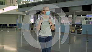 Woman in mask at empty airport at check in in coronavirus quarantine isolation, returning home, flight cancellation