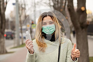 Woman in mask feeling protecting from the coronavirus, Covid2019 holding hands sanitizer showing like thumbs up fingers gesture photo