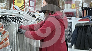 Woman in a mask and gloves buys clothes in a mall