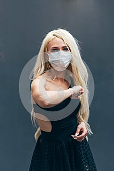 Woman in a mask greets the viewer with her elbows