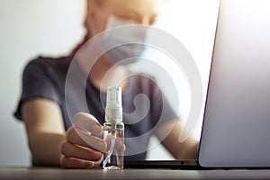 Woman in mask and hand with sanitizer alcohol bottle near laptop. Coronavirus covid-19 prevention at workplace or home during quar