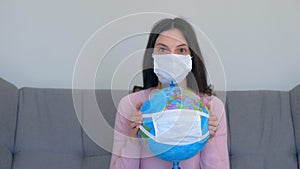 Woman in mask holding globe in mask in hands, pandemic quarantine.