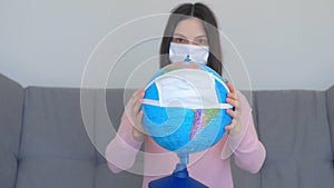 Woman in mask holding globe in mask in hands, pandemic quarantine.