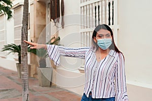 Woman with mask holding shopping bags in hand and smiling while hailing cab. Waiting for cab after a long day of shopping