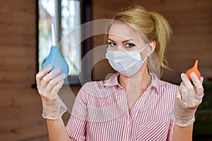 A woman in a mask holds an enema in her hands. bowel lavage