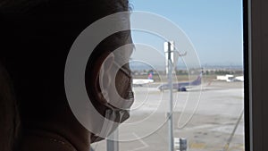 Woman In Mask Looks Out Of Airport Window At Plane During Pandemic Covid-19