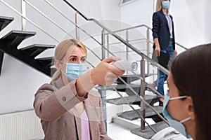 Woman in mask measuring temperature of employee with noncontact thermometer at office reception photo