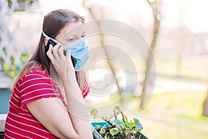 Woman with mask is out to home terrace using mobile phone during quarantine due to coronavirus covid19 pandemic