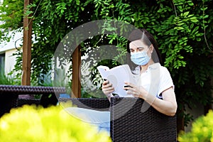 A woman in a mask is reading a book while sitting in a cafe.