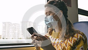 Woman in mask surfs internet with cellphone in transport