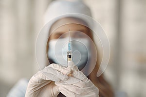 Woman in a mask and uniform holding a syringe in her hands