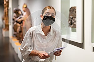 Woman in mask visiting exhibit at sculpture hall in museum