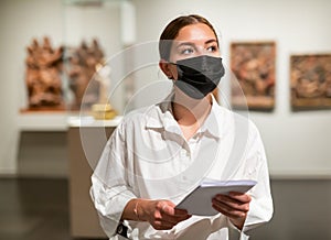 Woman in mask visiting exhibit at sculpture hall in museum