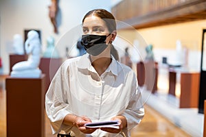 Woman in mask visiting exhibit at sculpture hall in museum