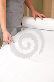 Woman massage therapist spreading disposable sheet on massage table