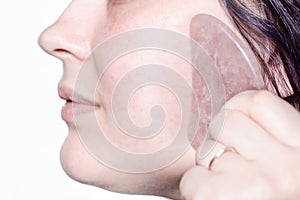 Woman massages cheek with quartz scraper close up