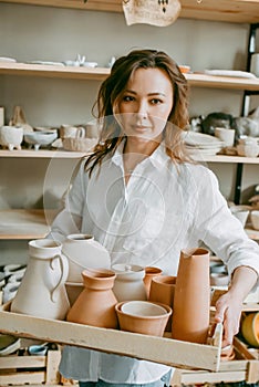 Woman master of pottery workshop carries clay products for firing