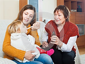 Woman with mature mother giving medicinal sirup to toddler